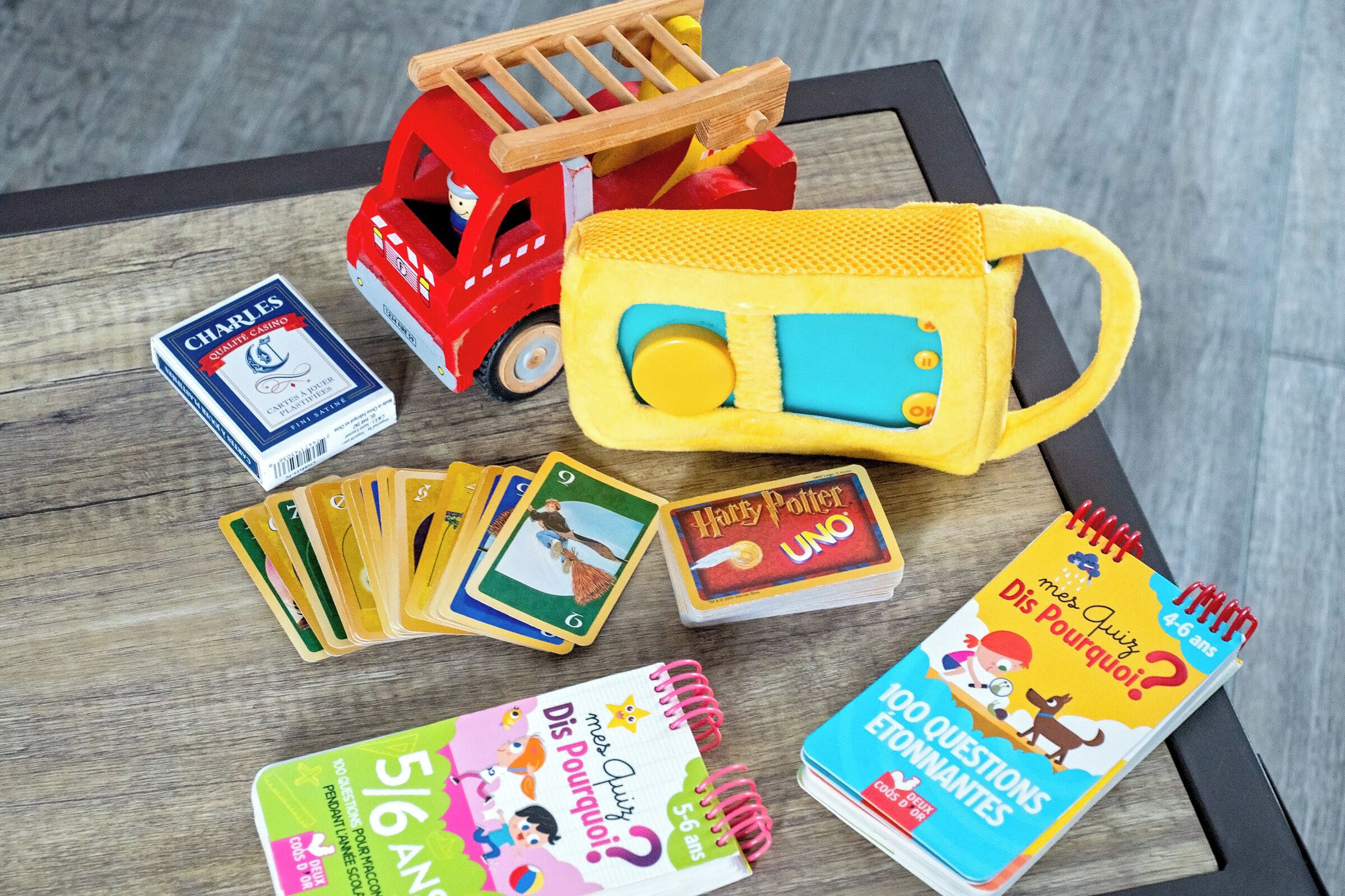 A table with various children's toys and books, including a toy fire truck, a yellow bus, and several Harry Potter UNO cards.