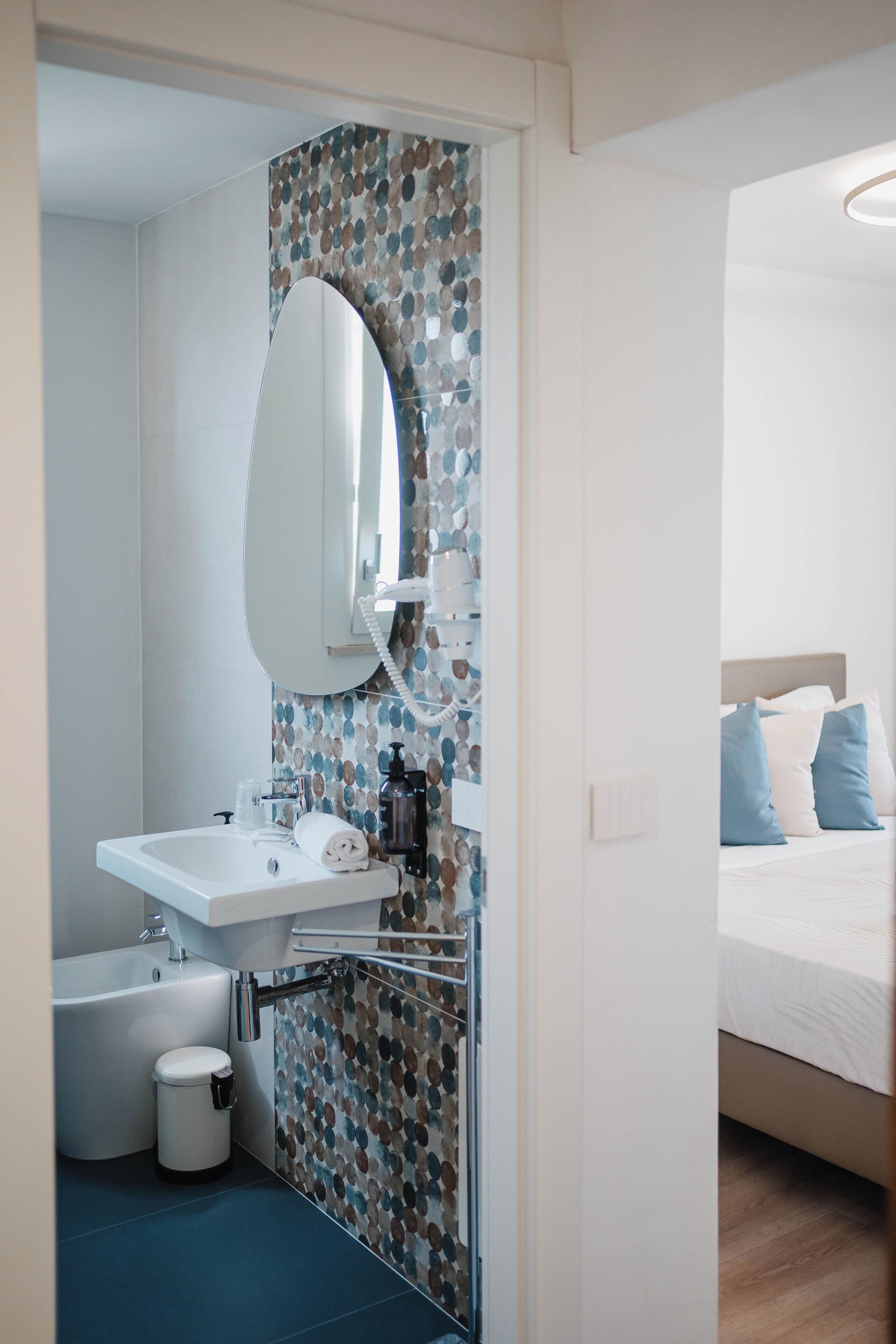 Un baño con lavamanos, espejo y retrete, y un dormitorio con cama y almohadas.