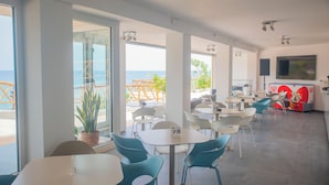 A spacious indoor area with multiple tables and chairs, large windows offering a view of the sea, and a television mounted on the wall. - Hotel Ficocella (Centola)