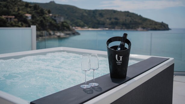 A hot tub with two champagne flutes and a bucket labeled "GEMINI" on a balcony overlooking a coastal landscape. - Hotel Ficocella (Centola)