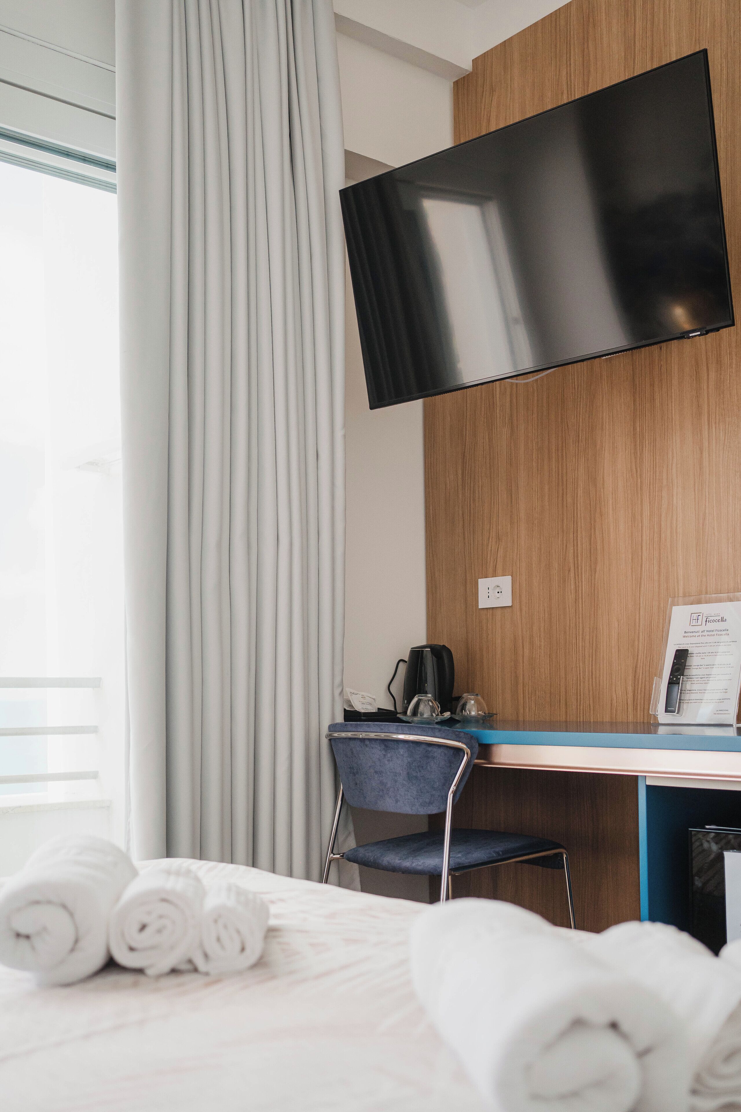 Hotelkamer met een bed, een bureau, een stoel, een flatscreen-tv en een raam met gordijnen.