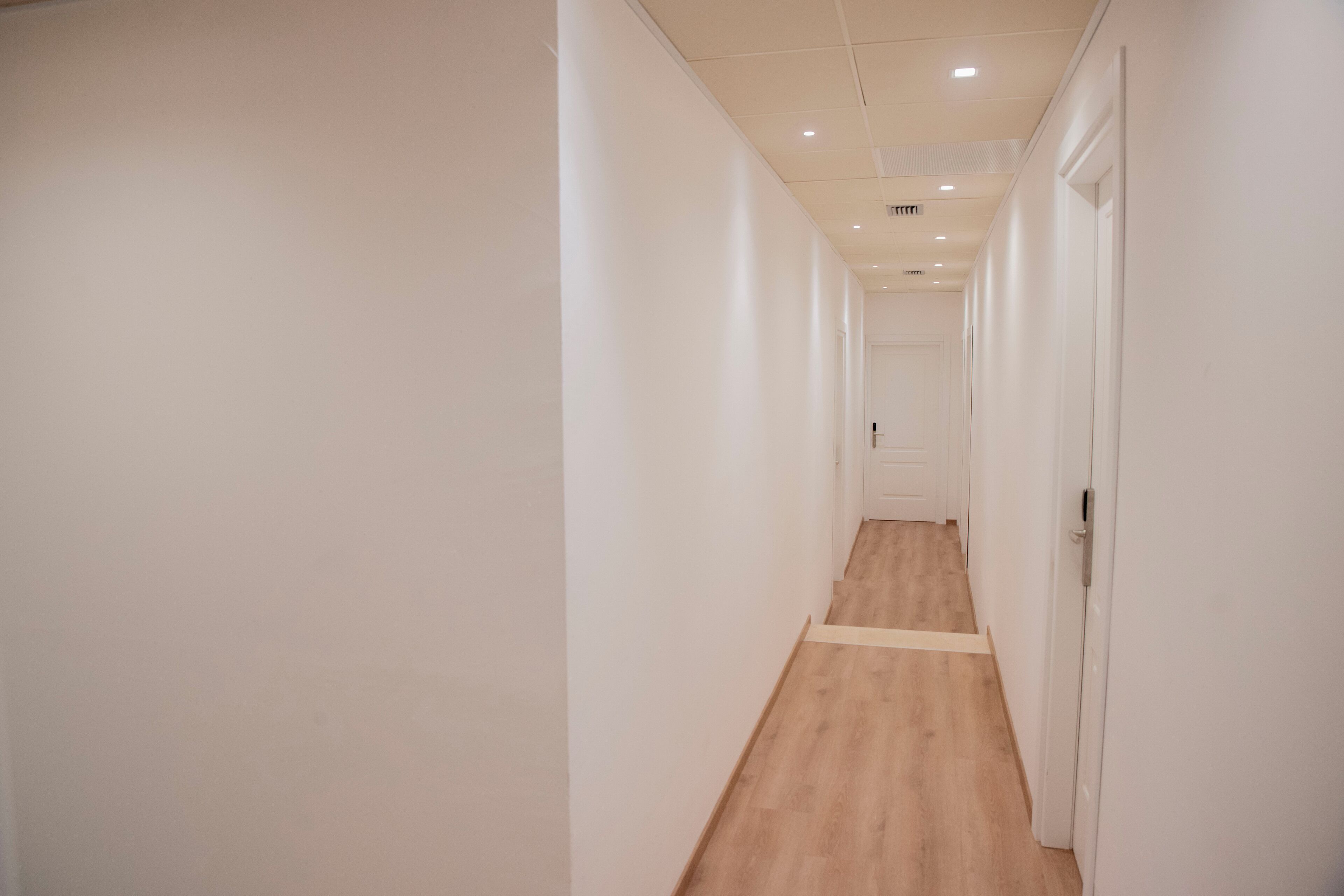 A narrow, well-lit hallway with wooden flooring and white walls.