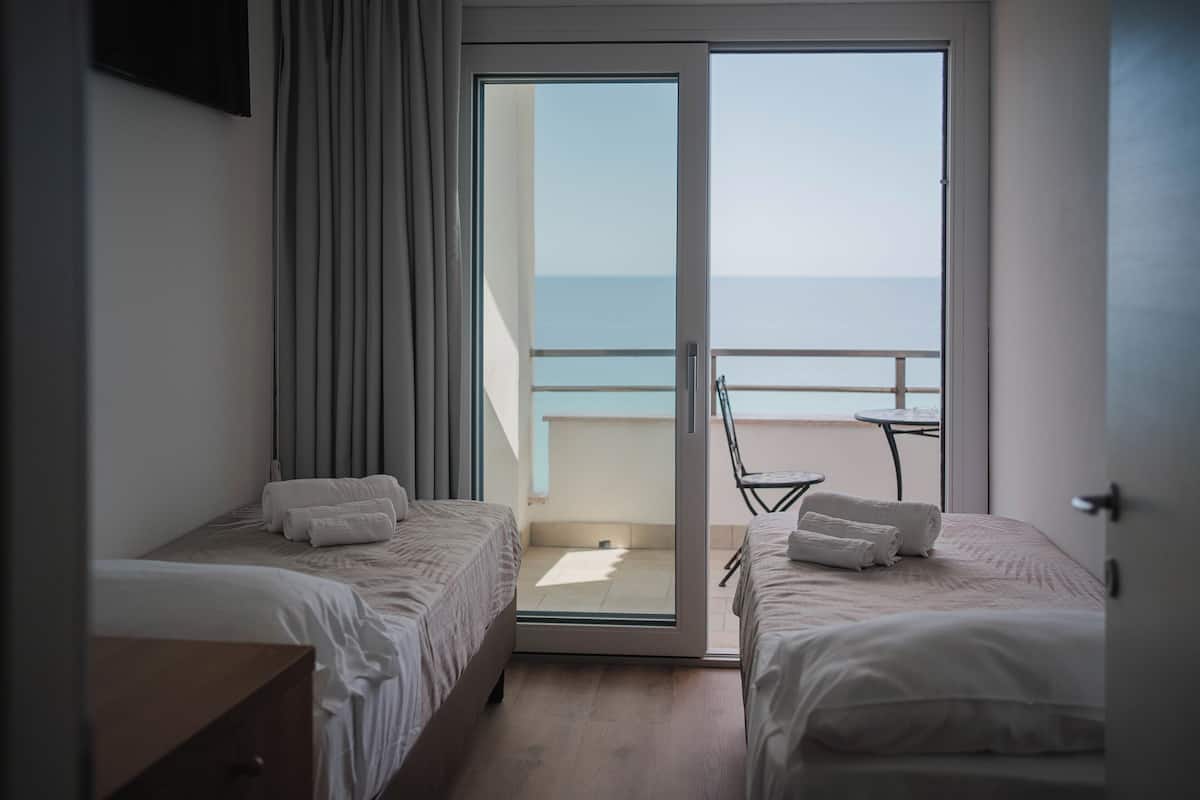 Ein Hotelzimmer mit zwei Betten, einem Balkon mit Tisch und Stühlen und Blick aufs Meer.