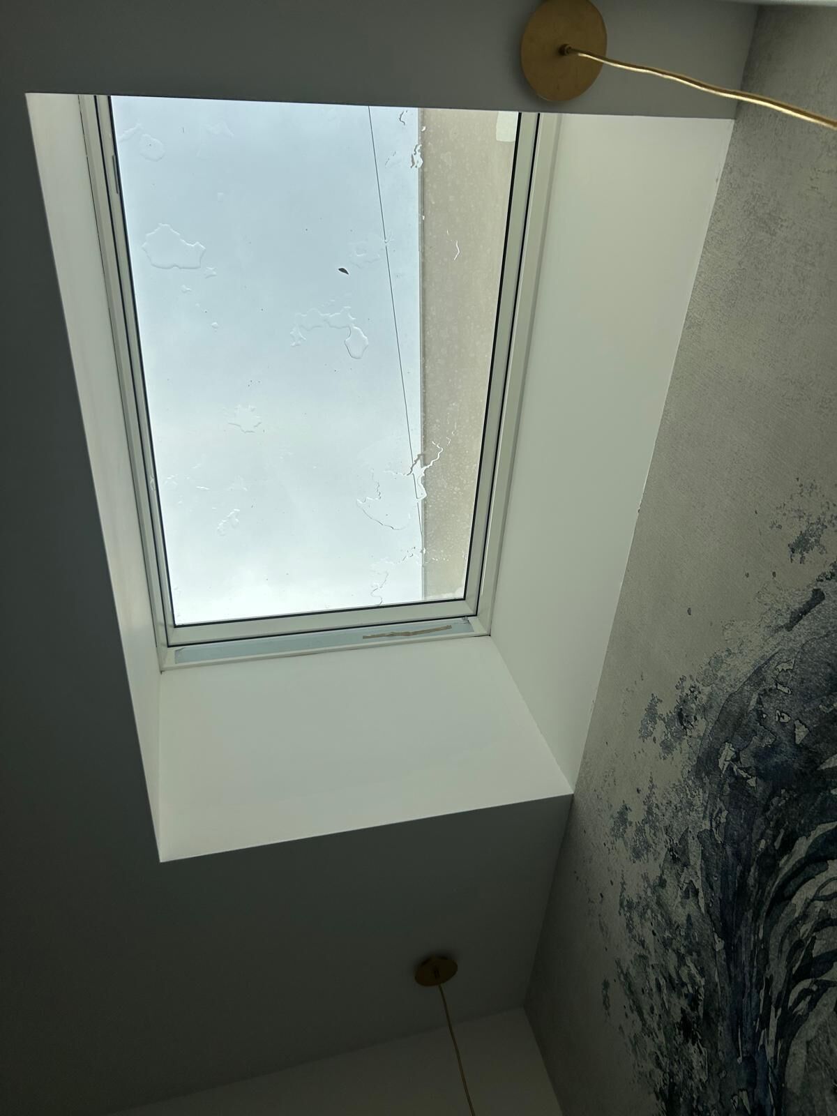 A skylight window in a room with a textured wall and a ceiling light fixture.