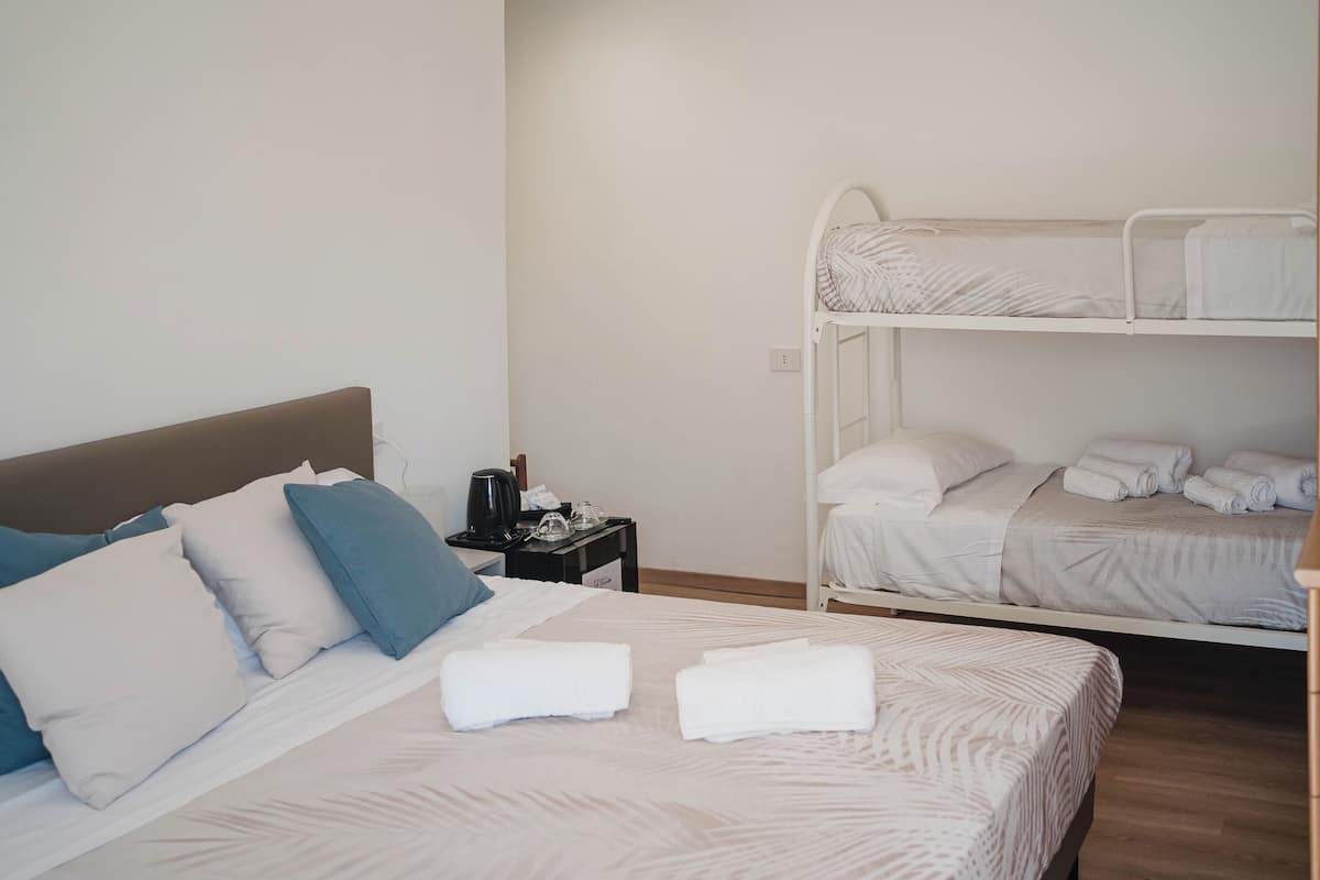 Ein Hotelzimmer mit einem Einzelbett, einem Stockbett, einem Nachttisch mit Kaffeemaschine und ordentlich gefalteten Handtüchern.