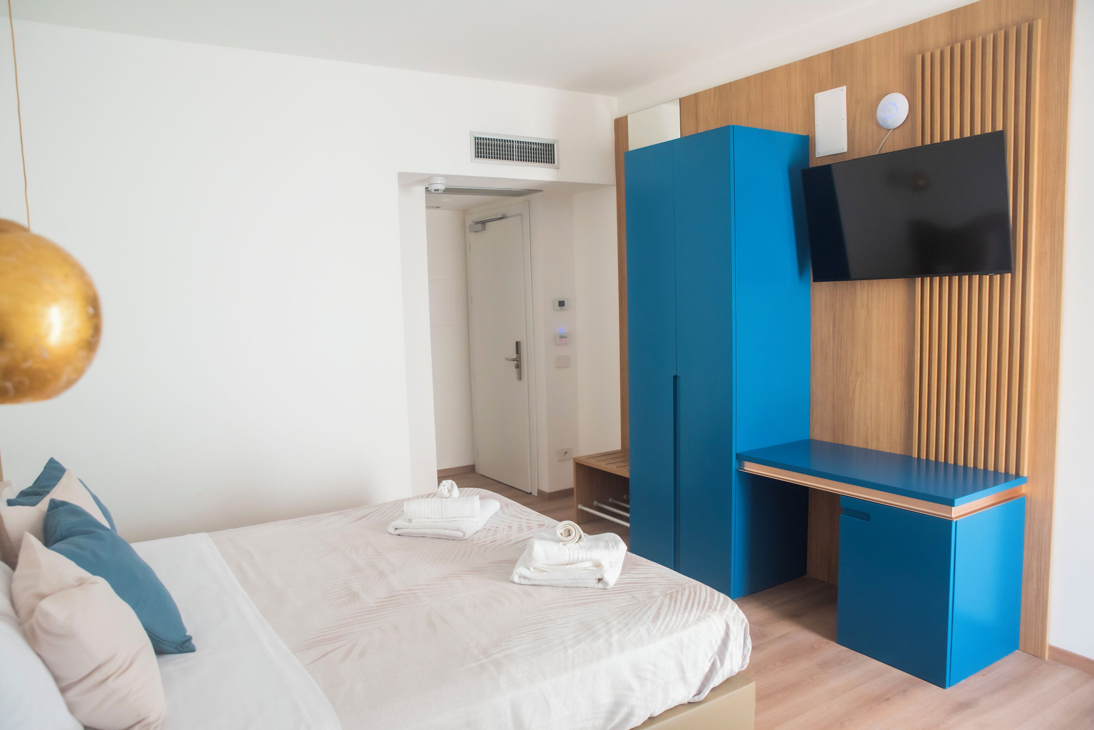 A modern hotel room with a bed, a desk, a TV, and a wardrobe.