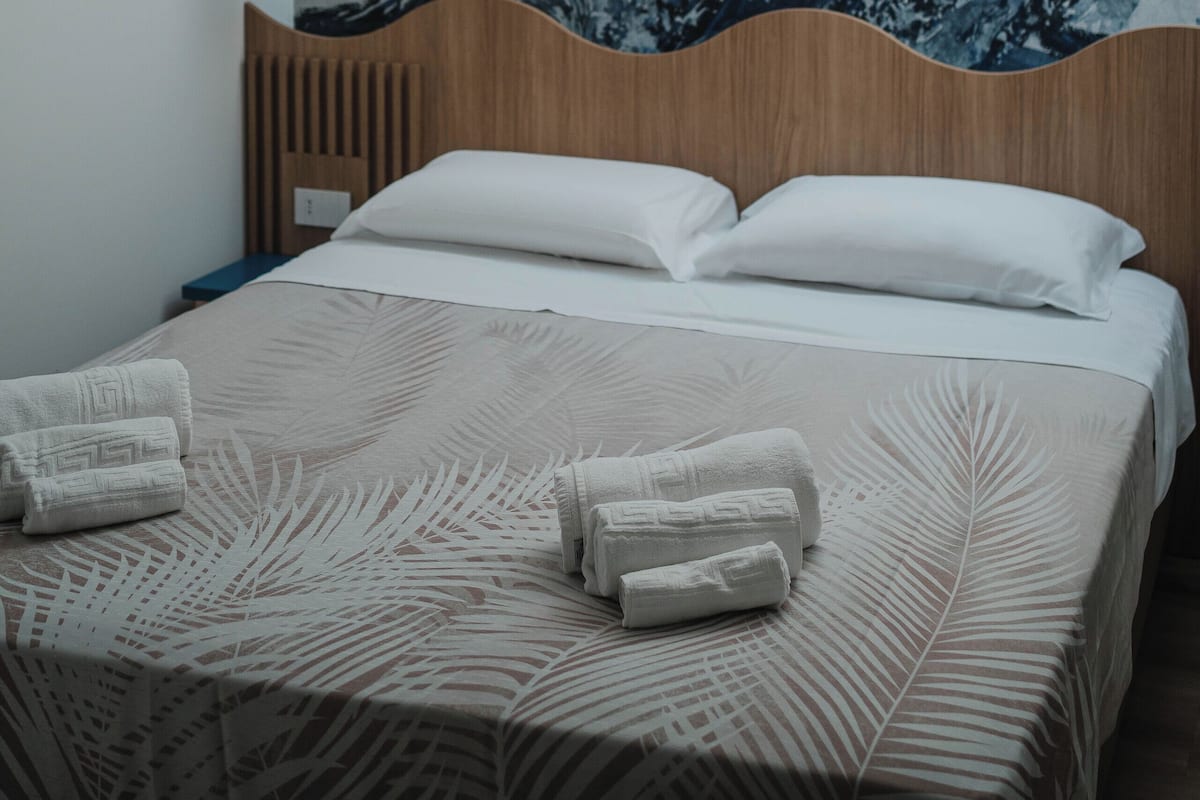 Ein modernes Hotelzimmer mit einer großen Wandmalerei im Wellen-Design, einem hölzernen Kopfteil, einem Bett mit weißen Leinentüchern und einer hängenden Pendelleuchte.