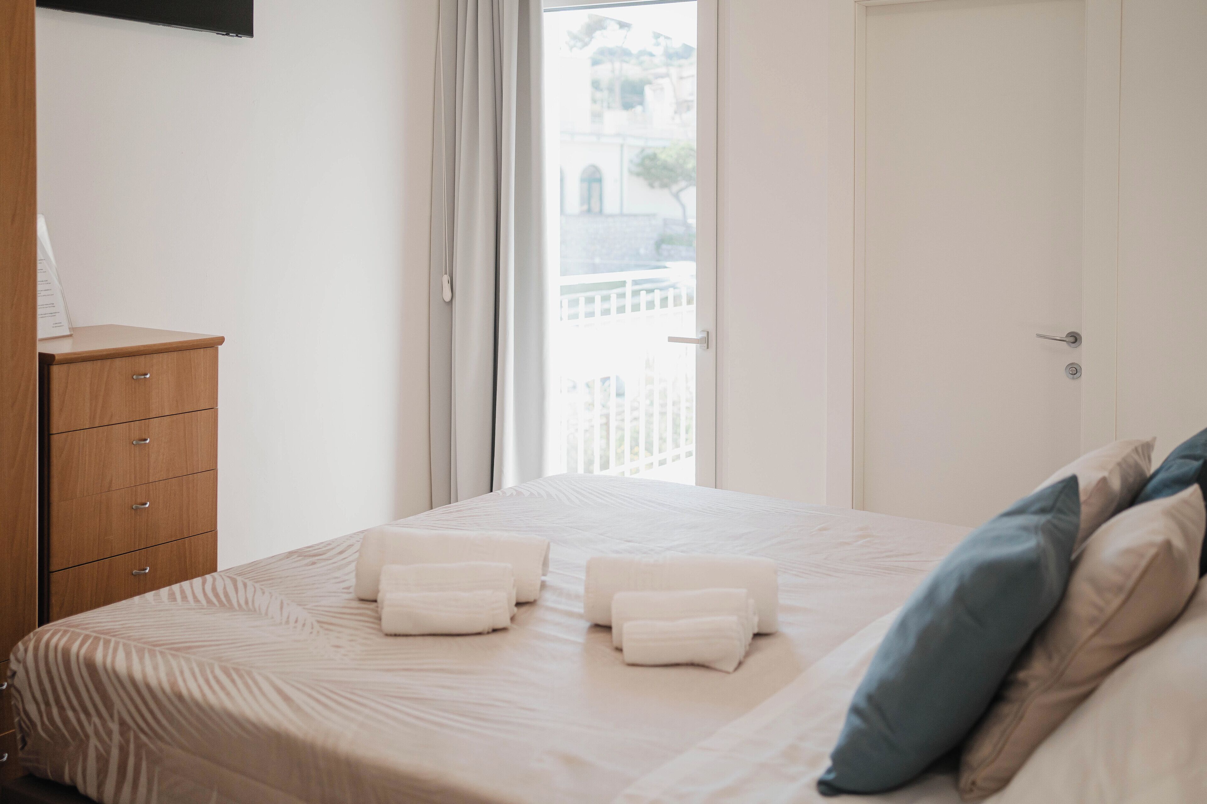 A hotel room with a bed, a wooden dresser, and a view of a balcony.