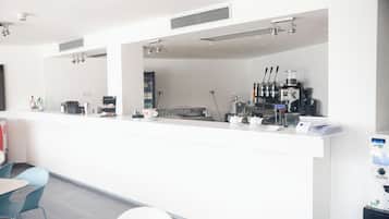Una cafetería moderna y bien iluminada, con un interior limpio y blanco, una barra con equipo para preparar café y sillas azules.