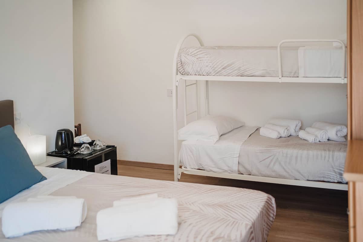 Ein Hotelzimmer mit Etagenbett, einem Einzelbett, einem Nachttisch mit Lampe und Holzboden.