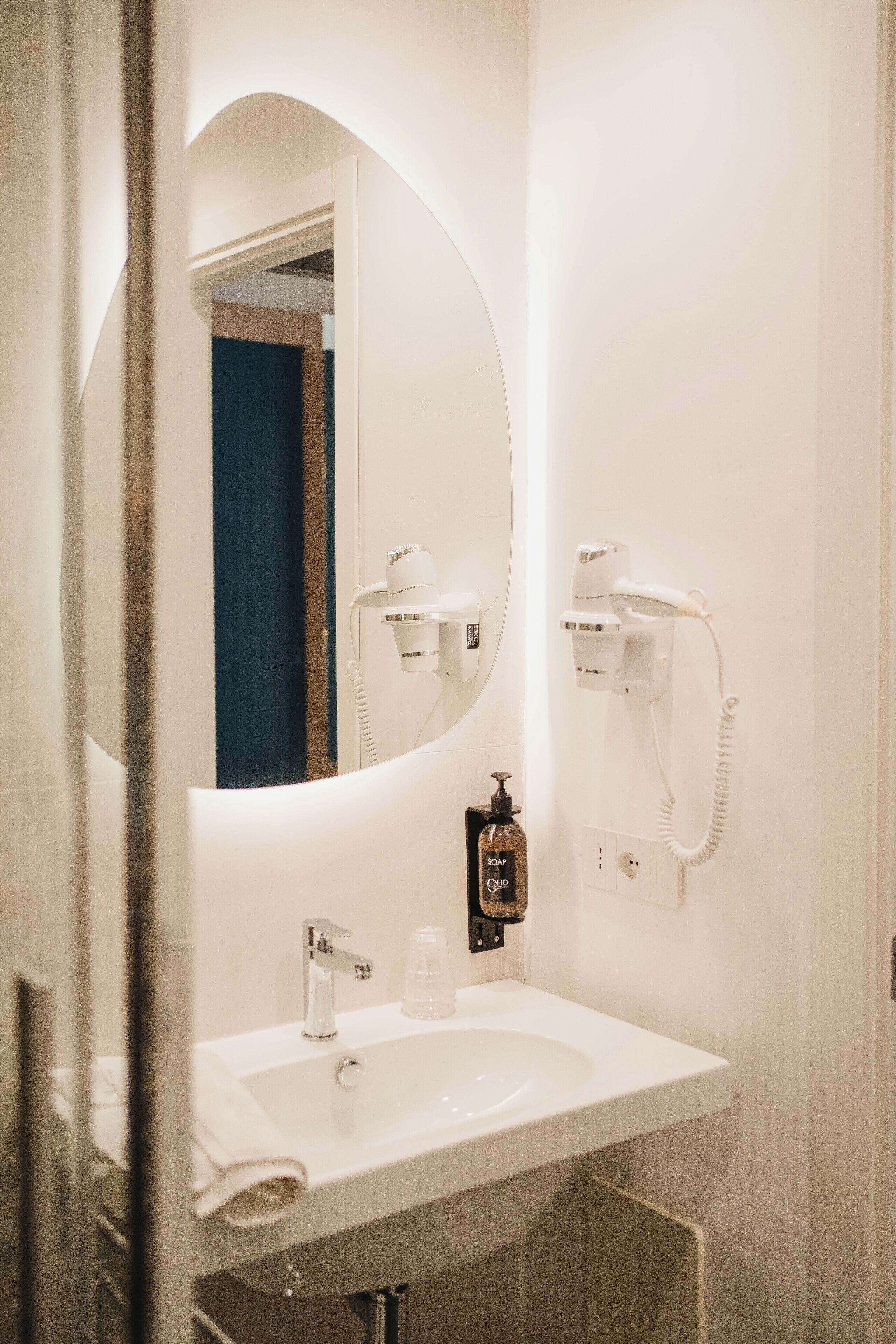 A bathroom with a white sink, a mirror, and two hair dryers mounted on the wall.
