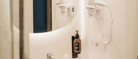A bathroom with a white sink, a mirror, and two hair dryers mounted on the wall.