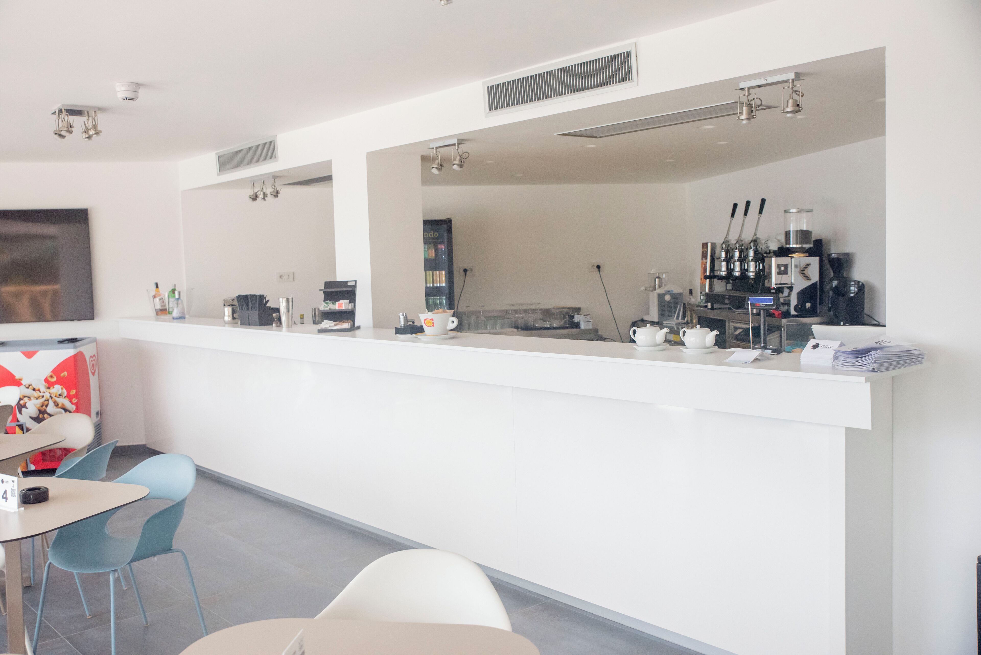 A modern cafe with a white counter, seating area with chairs, and a coffee machine.