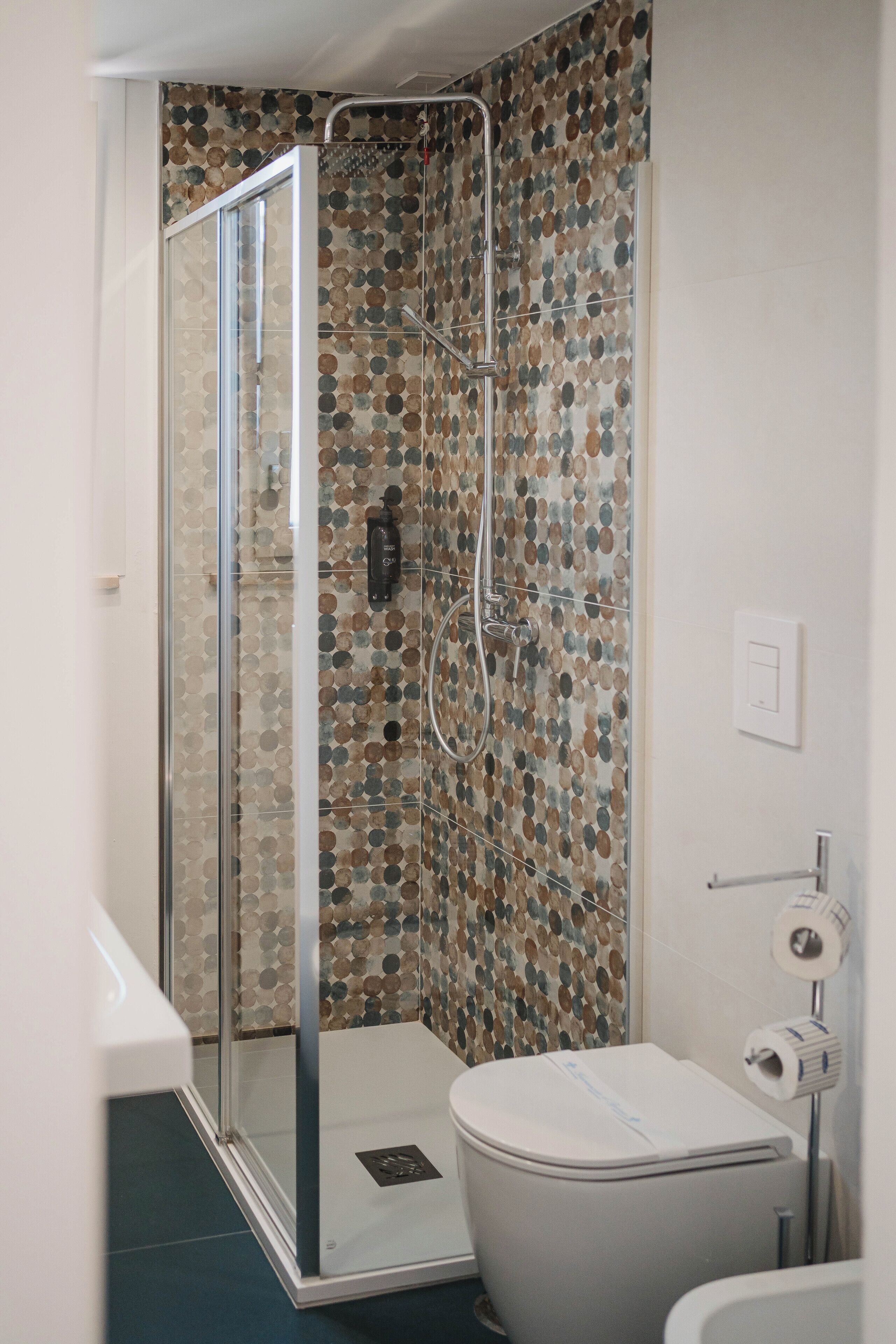 A bathroom with a shower enclosure, toilet, and a wall-mounted toilet paper dispenser.