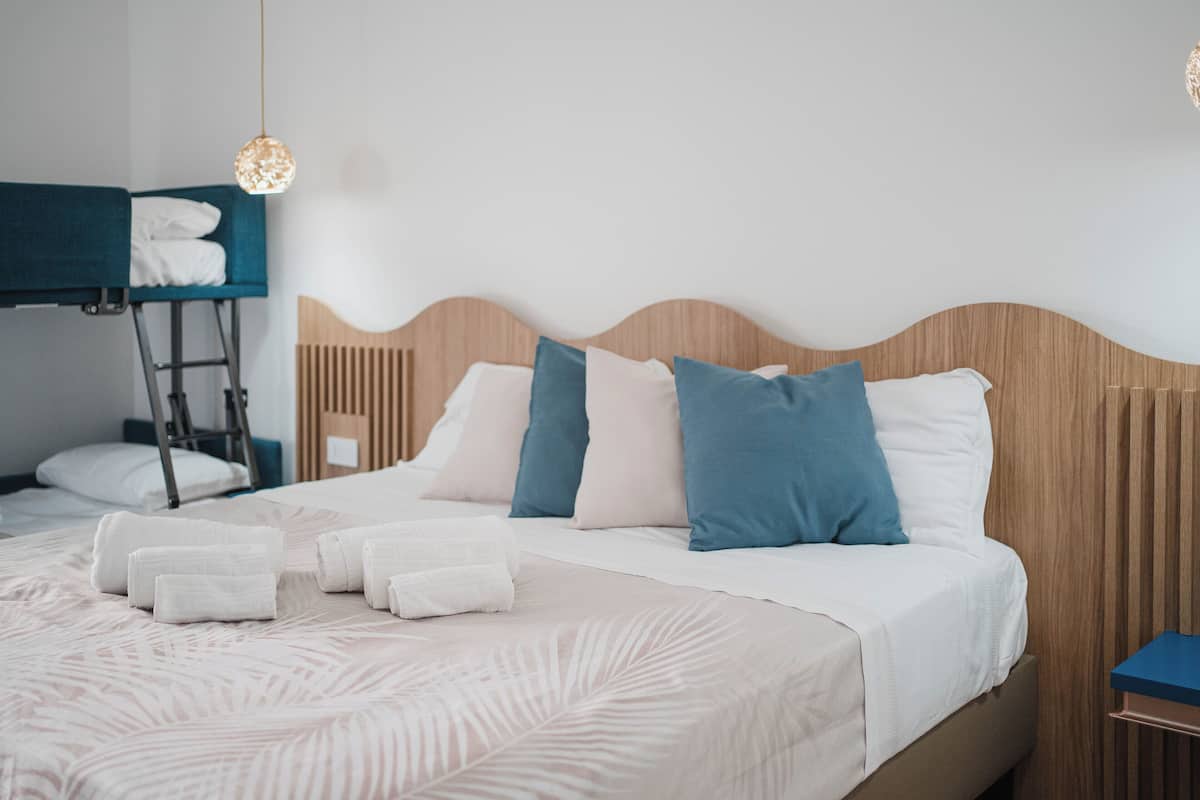 Ein ordentlich bezogenes Bett mit weißen und blauen Kissen, einem hölzernen Kopfteil und einem Hochbett darüber.