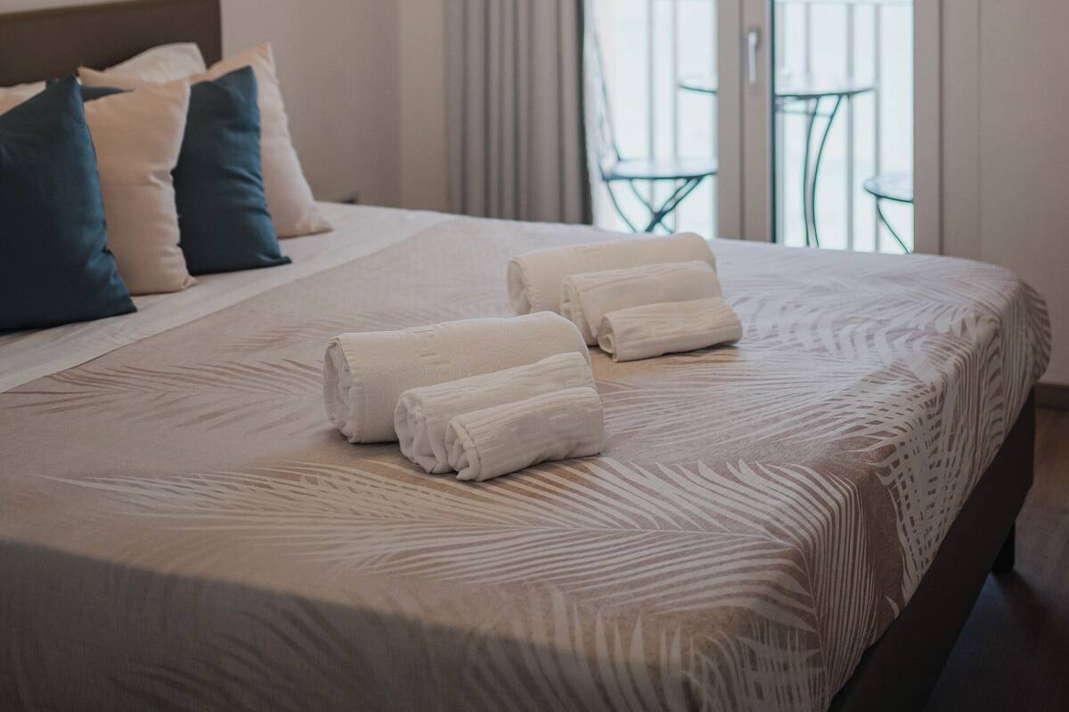 Ein Hotelzimmer mit Bett, Kissen, einem Balkon mit Blick und einer Deckenleuchte.