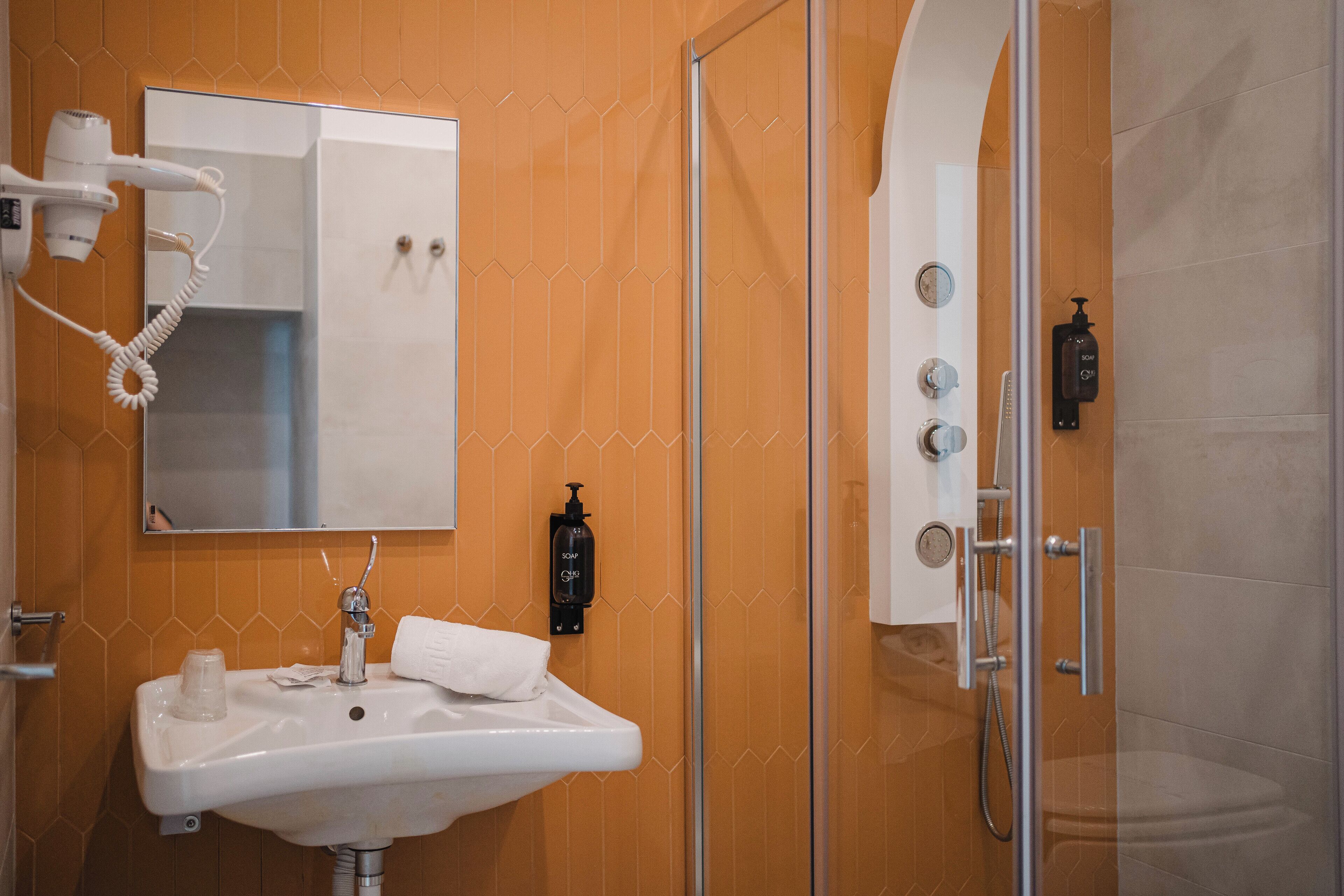 A bathroom with a white sink, a mirror, a hairdryer, and a glass shower enclosure.