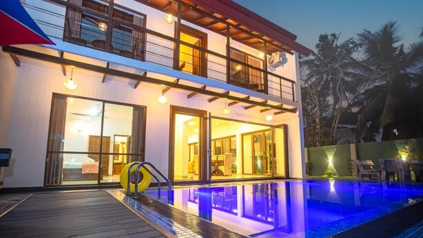 A two-story building with a swimming pool, large glass doors, and a balcony. - Villa Senaya (Galle)