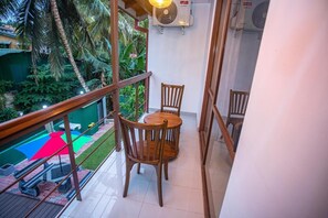 A balcony with a wooden table and chairs, a red umbrella, and a view of a pool and greenery. - Villa Senaya (Galle)