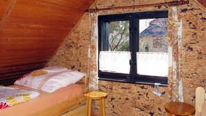 Una habitación acogedora con techo de madera, una cama con ropa de cama floral, un taburete de madera y una ventana con vista a un edificio.