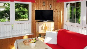 Una habitación acogedora con un sofá rojo, un televisor sobre un mueble de madera y una mesa con un arreglo floral.