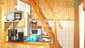 Una cocina rústica con vigas de madera, una escalera de madera, una cafetera, un microondas y un fregadero.