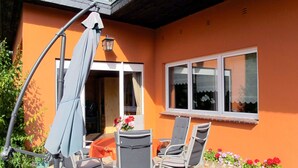 En udendørs terrasse med to stole og et bord, en parasol og et vindue med udsigt til himlen.