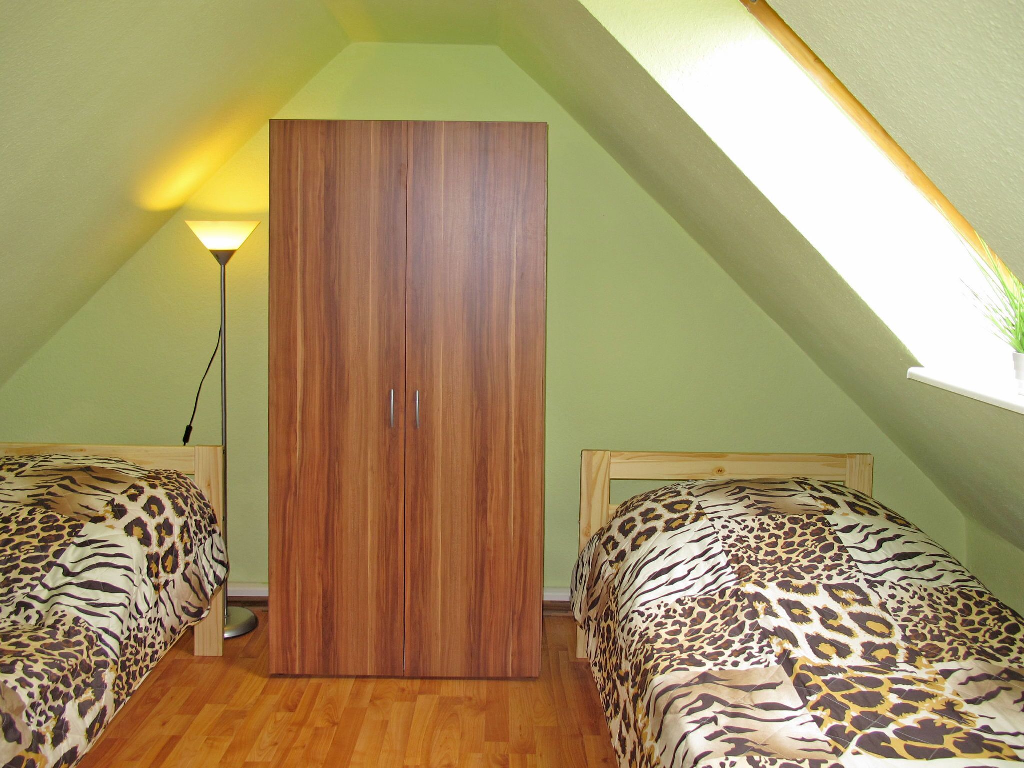 Une chambre avec une armoire en bois, deux lits avec du linge de lit à motifs léopard, une lampe sur pied et une lucarne.