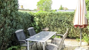 En udendørs terrasse med et bord og fire stole, omgivet af en hæk.