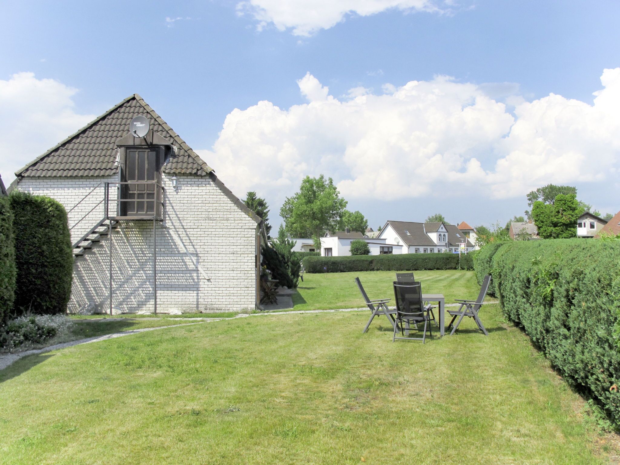 A brick building with a satellite dish, a grassy yard, and a row of houses in the background.