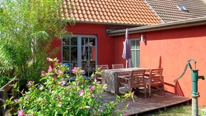 A red house with a tiled roof, a wooden deck, and a table with chairs.