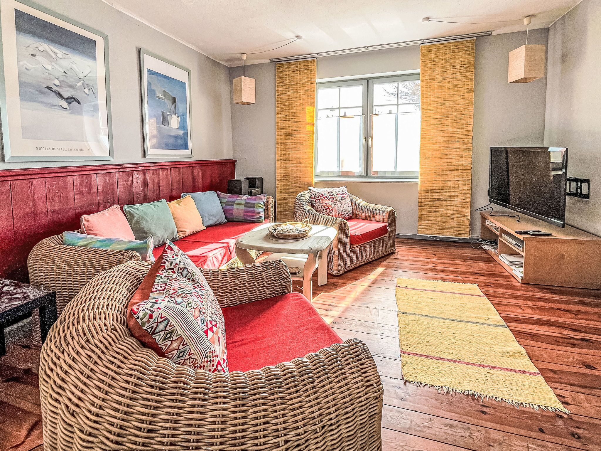 A living room with wicker furniture, a red sofa, a television, and artwork on the wall.