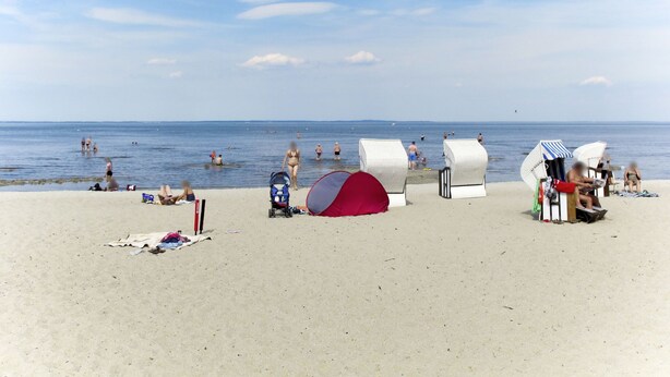 A beach with beach huts, a red tent, and people swimming and relaxing.