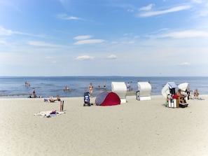 A beach with beach huts, a red tent, and people swimming and relaxing.