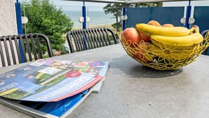 Une table avec un panier de fruits contenant des bananes et des pommes, un menu et une vue sur la mer.