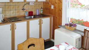 Une cuisine compacte avec des meubles en bois, un évier, une petite cuisinière et une fenêtre donnant sur une clôture rouge et de la verdure.