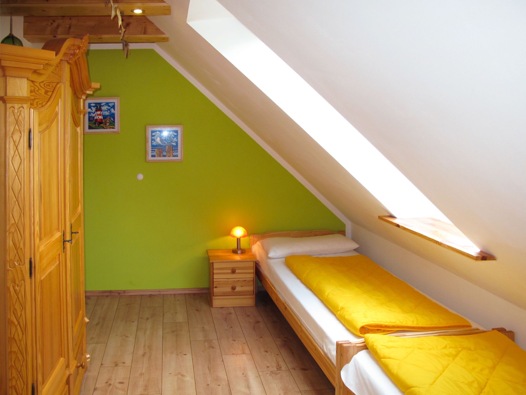 A small, single-bed room with a sloped ceiling, wooden flooring, and a green wall.