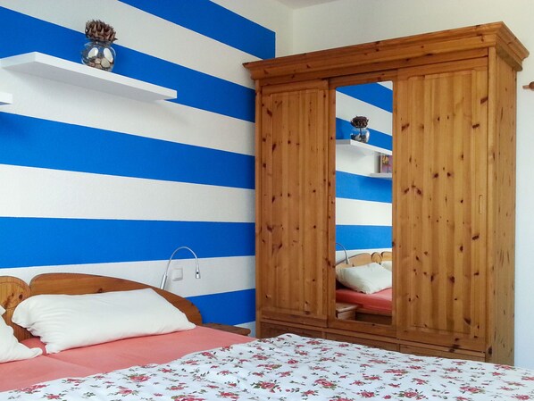 A bedroom with a bed, a wooden wardrobe, and a wall with blue and white stripes. - Kapitänskajüte by Interhome (Breege)