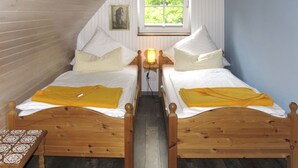 A room with two wooden beds, a window with a view of greenery, a small table, and a wall-mounted picture. - Hühnerhaus by Interhome (Schwarbe)