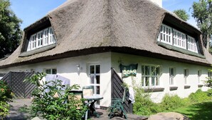 Ein traditionelles Haus mit Strohdach und weißem Anstrich, zwei Fenster mit weißen Rahmen sowie ein Schild mit der Aufschrift 'Bela'.
