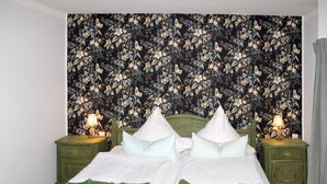 Ein Bett mit floralem Wandteppich, grünem Kopfteil und zwei Nachttischen mit Lampen.