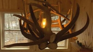 A rustic interior with wooden walls, a chandelier made of antlers, and a window with a view of trees. - Wolf Creek (Edgewood)