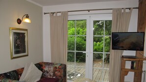 En stue med en farverig sofa, et fjernsyn på et træstel og en skydedør til et udendørs område.