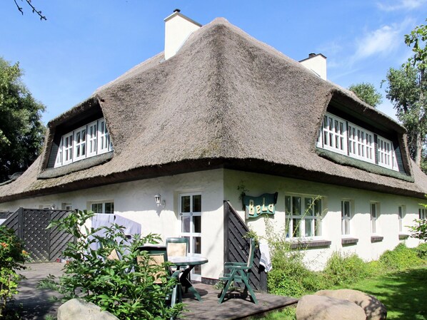 Ein traditionelles Haus mit Strohdach und weißem Anstrich, zwei Fenster mit weißen Rahmen sowie ein Schild mit der Aufschrift 'Bela'.