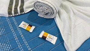A bed with a blue quilted cover, a rolled white towel, and two small packets on the bed. - Pousada Territorial  (Cairu)