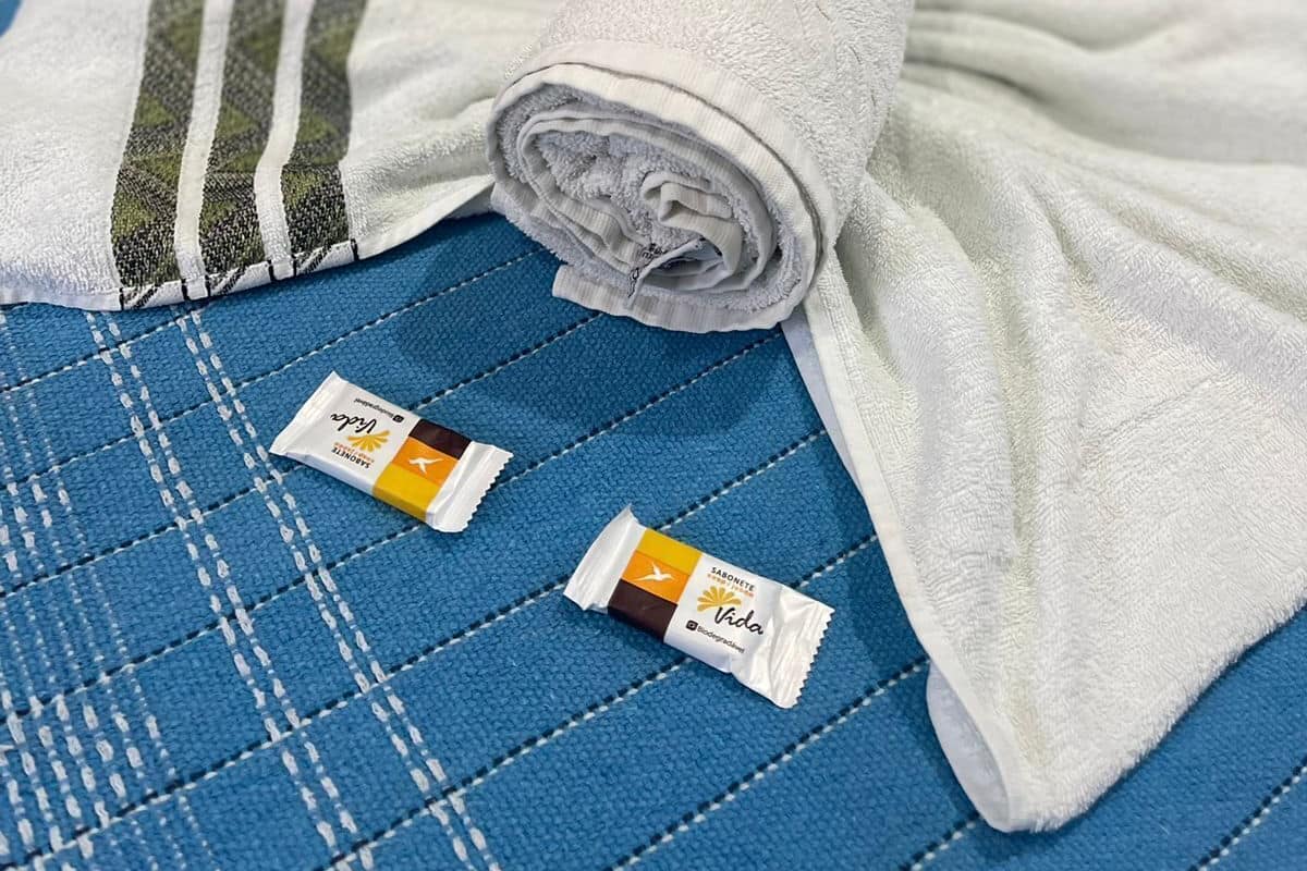 Ein Bett mit einer blauen gesteppten Decke, einem aufgerollten weißen Handtuch und zwei kleinen Packungen auf dem Bett.
