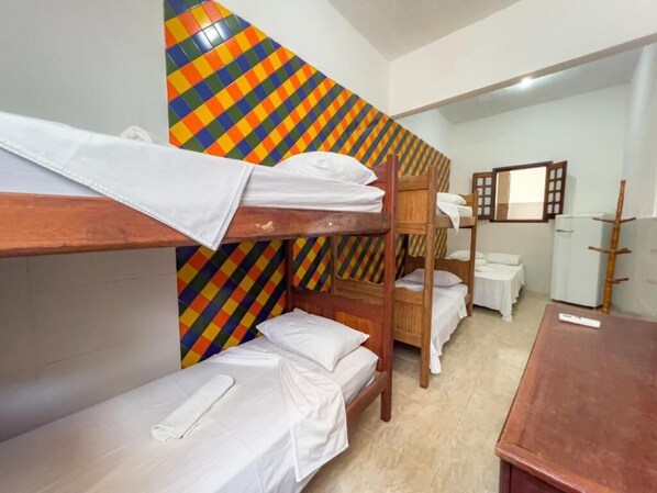 A dormitory room with bunk beds, a mirror, a small table, and a colorful wall pattern. - Pousada Territorial (Cairu)