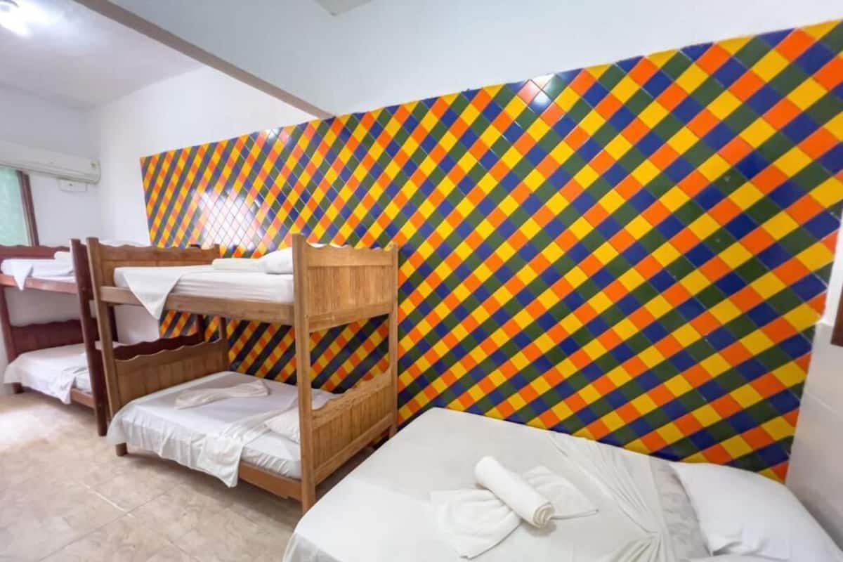 Ein Hotelzimmer mit Stockbetten, einer Wand mit bunten geometrischen Mustern und einem ordentlich bezogenen Bett mit Handtuch.