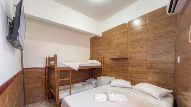 A hotel room with a bunk bed, a desk with a chair, a flat-screen TV, and a wooden accent wall. - Pousada Territorial  (Cairu)