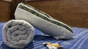 A bed with a rolled white towel and a white pillow with a green stripe. A television is mounted on the wall in the background. - Pousada Territorial  (Cairu)